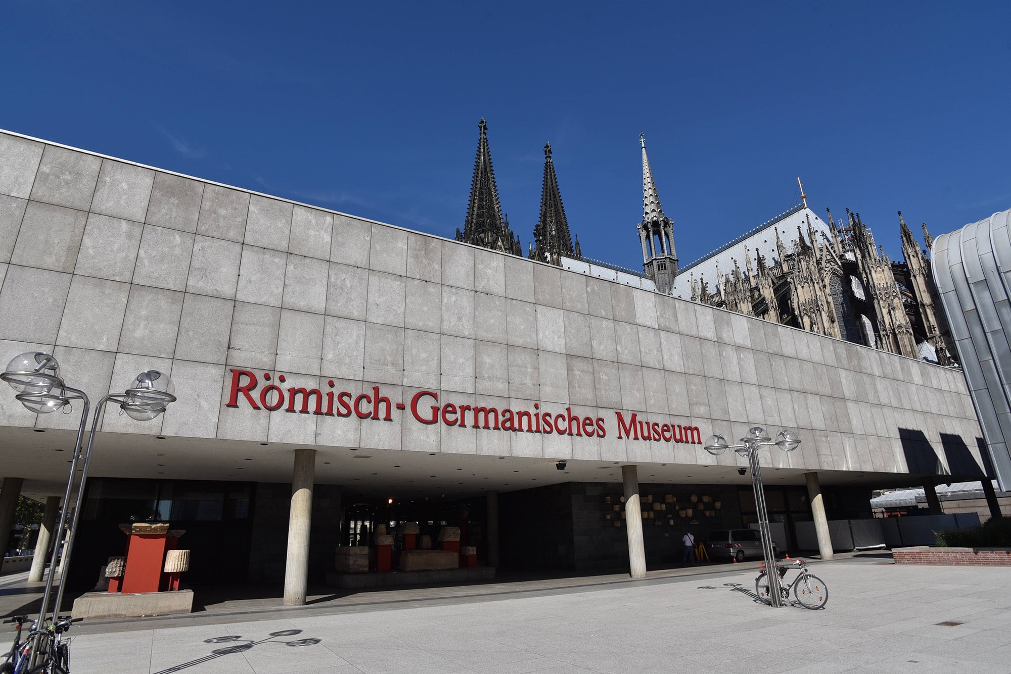 Das Foto zeigt die Außenfassade des Römisch-Germanischen Museum vor der Kulisse des Kölner Doms.