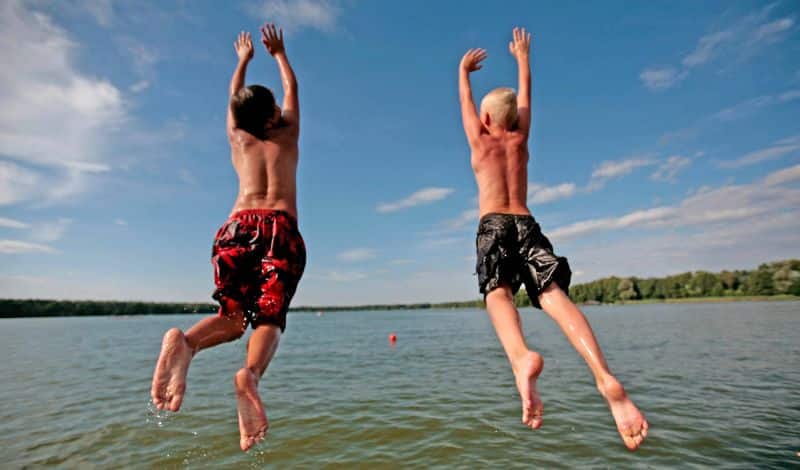 Zwei Jungs springen in das Wasser eines Badesees.