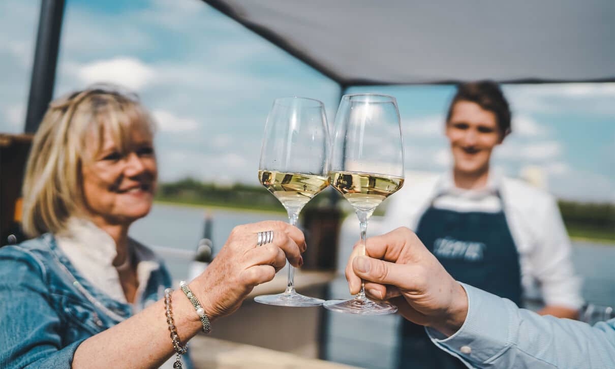 Zwei Gläser Weißwein, mit denen angestoßen wird.