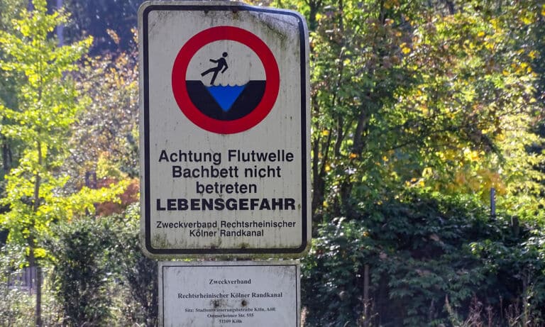 Mit einem Hinweis wird vor dem Aufkommen einer Flutwelle in einem Bach gewarnt.