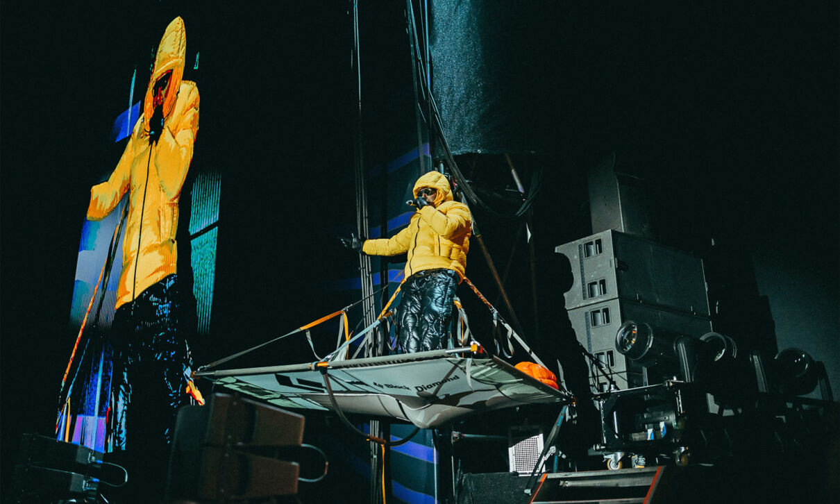 Ein Mitglied der Hiphop-Band Deichkind in einer gelben Winterjacke auf der Bühne.