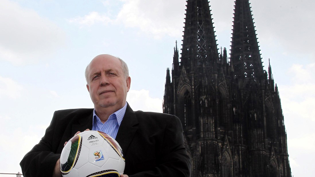 Das Foto zeigt Reiner Callmund mit einem Fußball in der Hand vor der Kulisse des Kölner Doms.