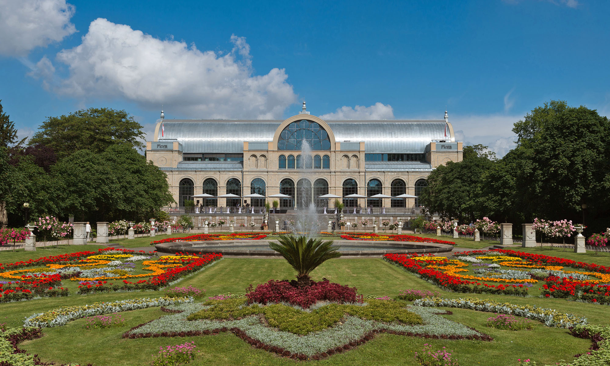 Blumenreicher Botanischer Garten und Park mit dem Gebäude der Flora im Hintergrund.