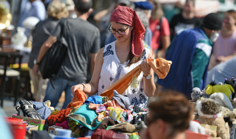 Frau stöbert auf einem Flohmarkt in einem Haufen Second-Hand-Bekleidung.