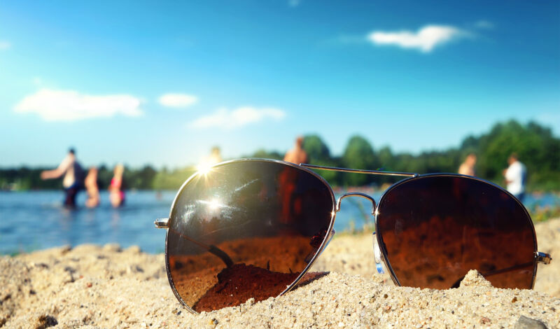 Eine Sonnenbrille liegt am Sandstrand eines Badesees.