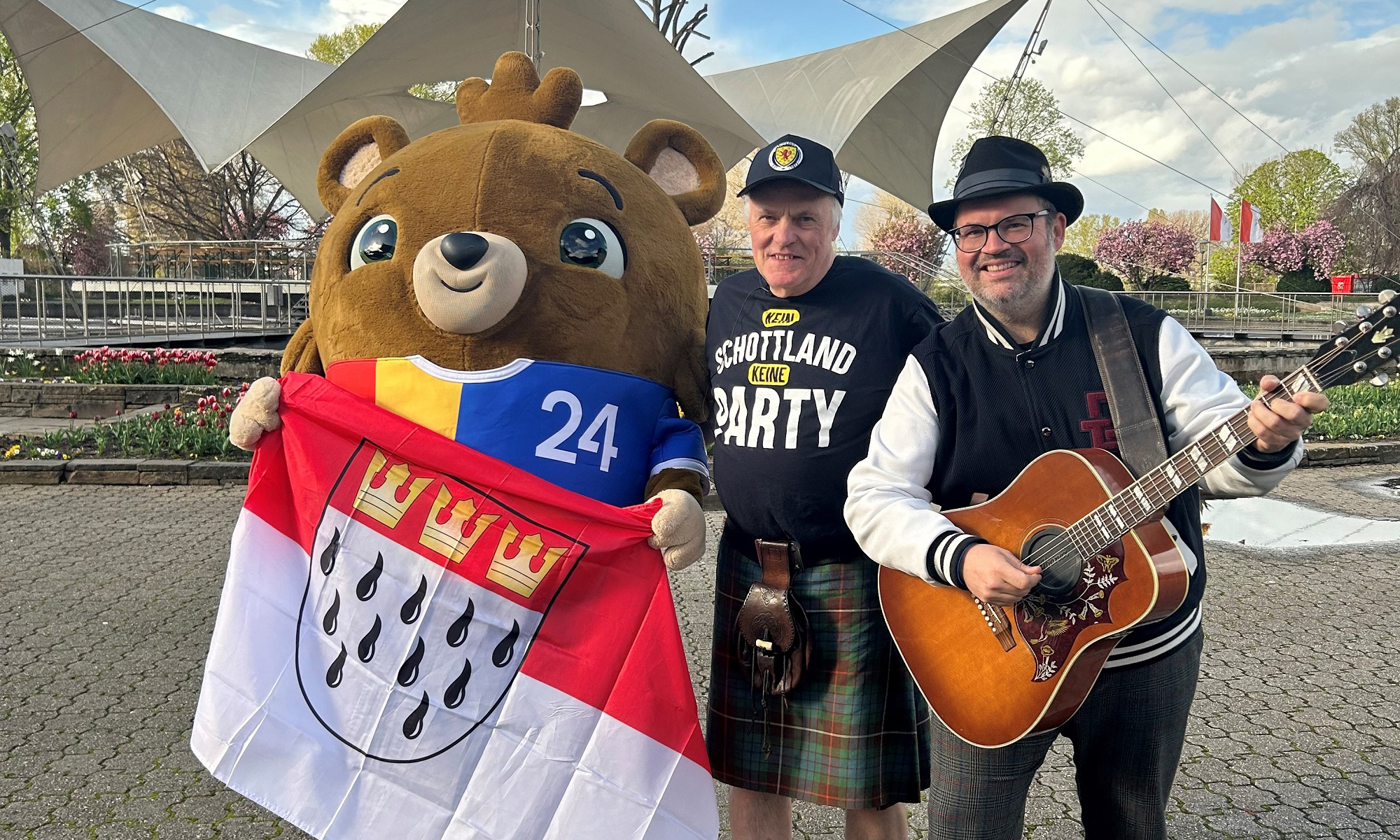 Der schottische Sänger Ted Christopher und Björn Heuser posieren mit EM-Maskottchen 2024 im Tanzbrunnen