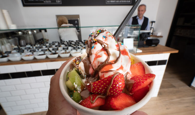 Ein Becher Frozen Yogurt mit Erdbeeren, Kiwis und Streuseln.