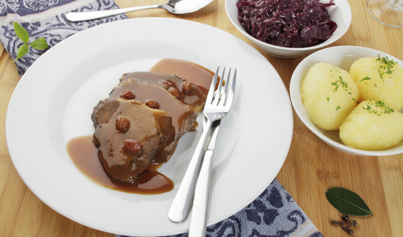 Das Foto zeigt auf einem Teller rheinischen Sauerbraten und daneben Klöße und Rotkohl.