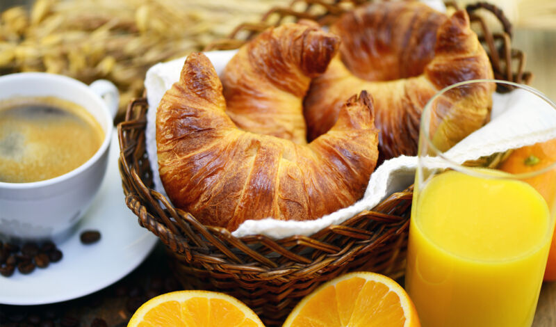 Mehrere Croissants in einem Körbchen, dazu Orangensaft.