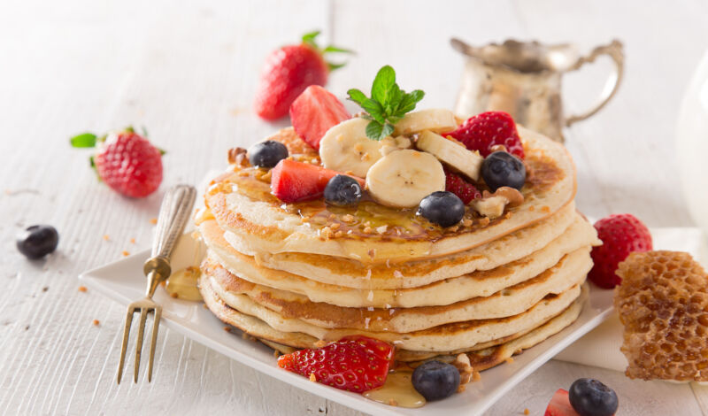 Eine große Portion Pancakes mit Früchten und Honig.