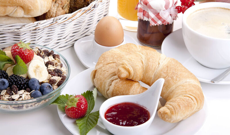 Ein gedeckter Frühstückstisch mit Croissant, Marmelade und mehr.