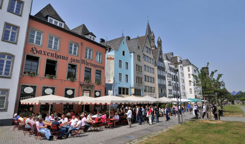 In der Außengastronomie der Lokale am Kölner Rheingarten sitzen Gäste unter Sonnenschirmen