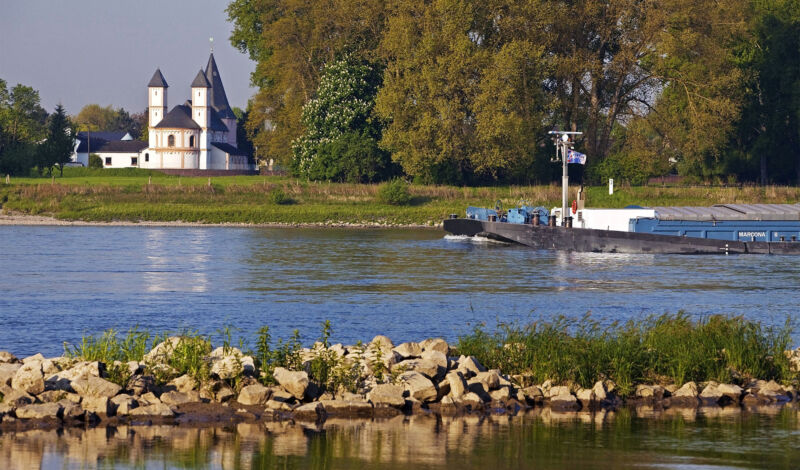 Ein Schiff fährt auf dem Rhein vorbei an der Kirche St. Amandus im Kölner Stadtteil Rheinkassel.