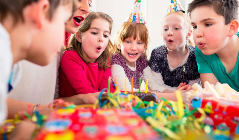 Kinder feiern einen Kindergeburtstag und blasen Kerzen aus