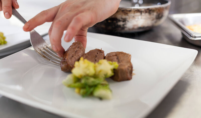 Ein Koch platziert Fleisch und Beilagen auf einem Teller.