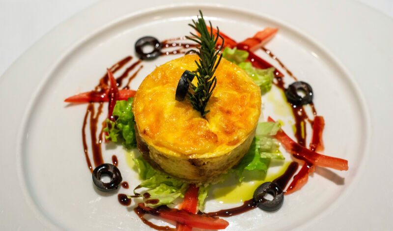 Eine Quiche in Form eines kleinen Törtchens auf einem Bett mit Salat, Paprika und Oliven.