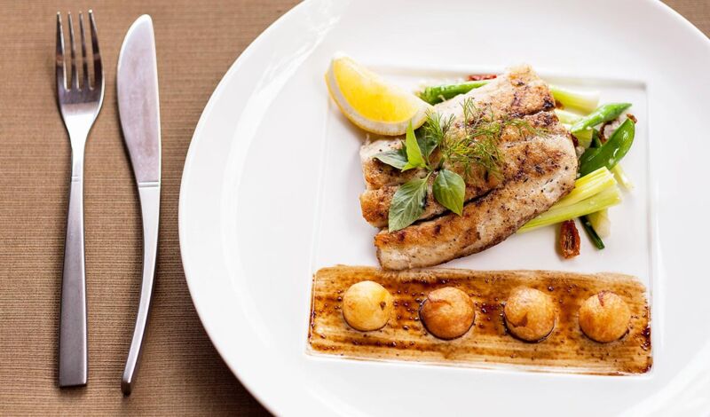 Gebratenes Fischfilet auf einem Bett von Sellerie und Zuckeschoten mit Kartoffelbällchen.