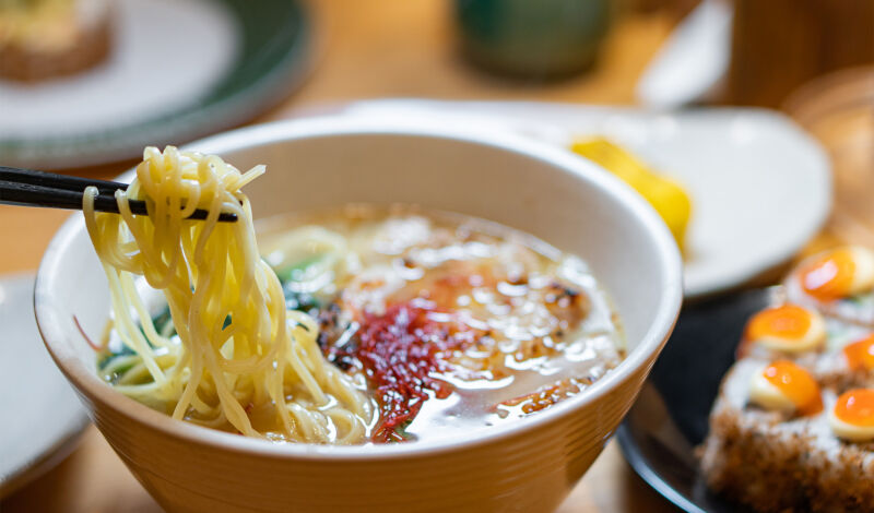 Ramen, japanische Nudeln, werden mit Stäbchen aus einer kleinen Schüssel gegessen.