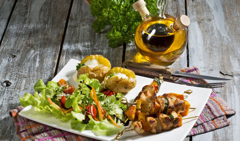 Ein Teller mit Salat, Fleischspieß und Ofenkartoffel, im Hintergund eine Flasche mit Öl.