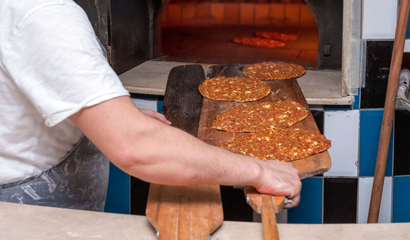 Ein Mann schiebt mehrere Lahmacun - türkische Pizza - in einen Backofen.