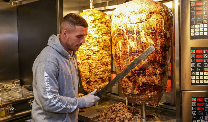 Lukas Podolski an einem Drehspieß für Döner in einem Imbiss