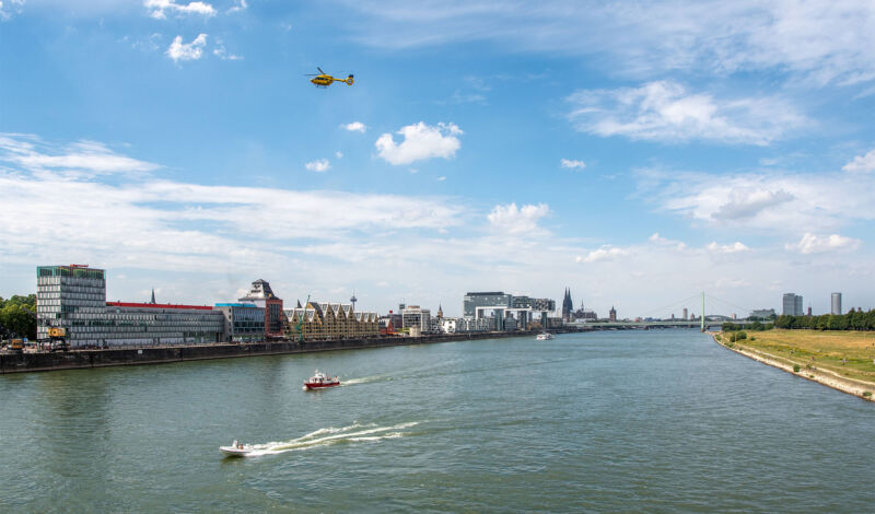 Ein Hubschrauber fliegt über den Rhein und den Kölner Rheinauhafen