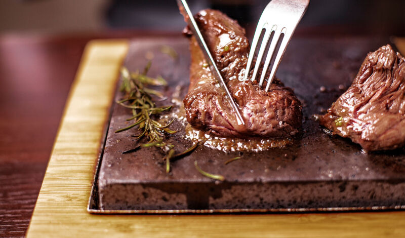 Ein Steak auf einem heißen Stein wird mit Messer und Gabel geschnitten.