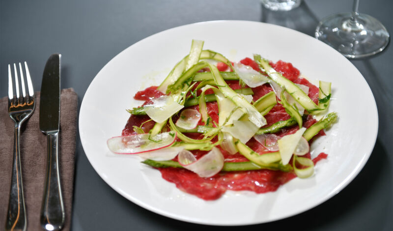 Carpaccio vom Rind mit grünem Spargel und Zitronenvinaigrette auf einem weißen Porzellanteller