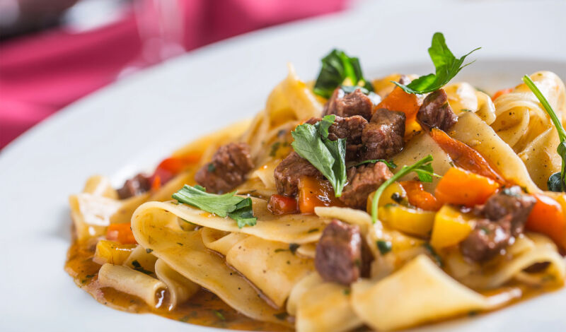 Pasta Pappardelle mit Fleisch auf einem weißen Teller.