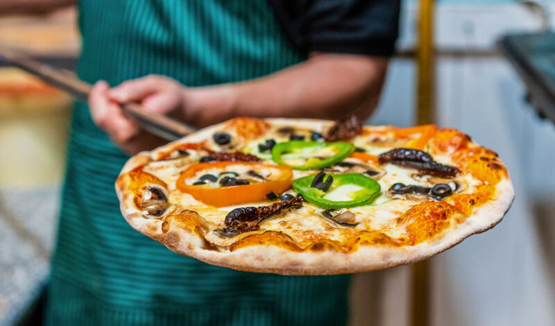 Ein Pizzabäcker holt eine fertige Pizza auf einem Blech aus dem Ofen