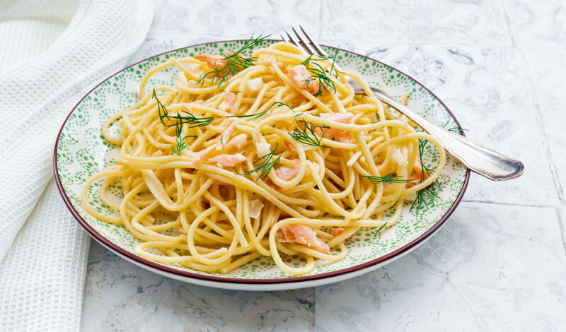 Ein Teller mit Spaghetti mit Lachs, in dem eine Gabel steckt.