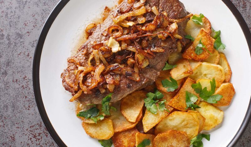 Ein Rostbraten mit Zwiebeln sowie mit Bratkartoffeln als Beilage