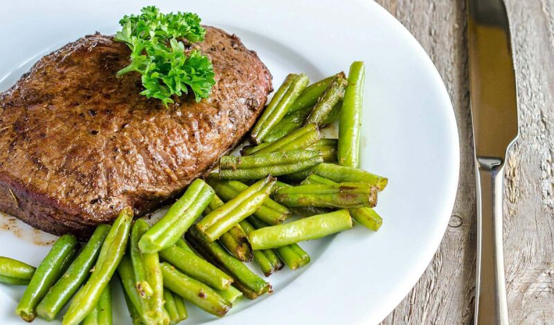 Ein Steak mit Bohnen auf einem weißen Porzellanteller.