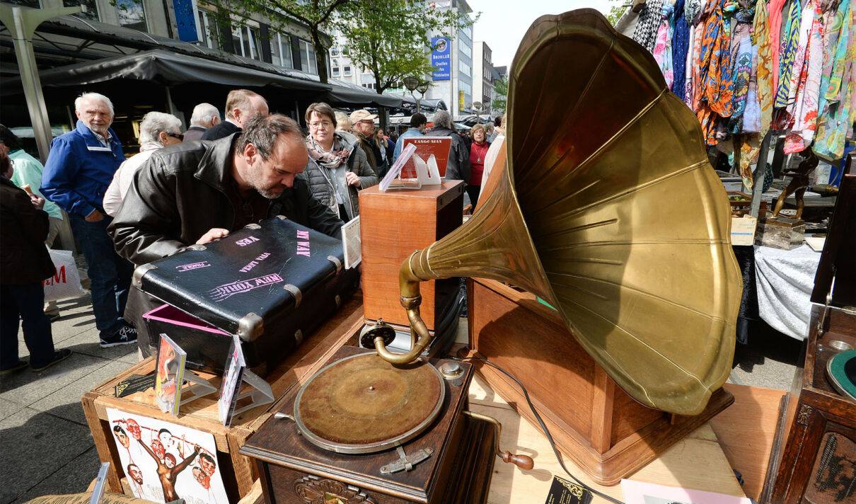 Ein Mann betrachtet die Auslage eines Händlers auf einem Antikmarkt.